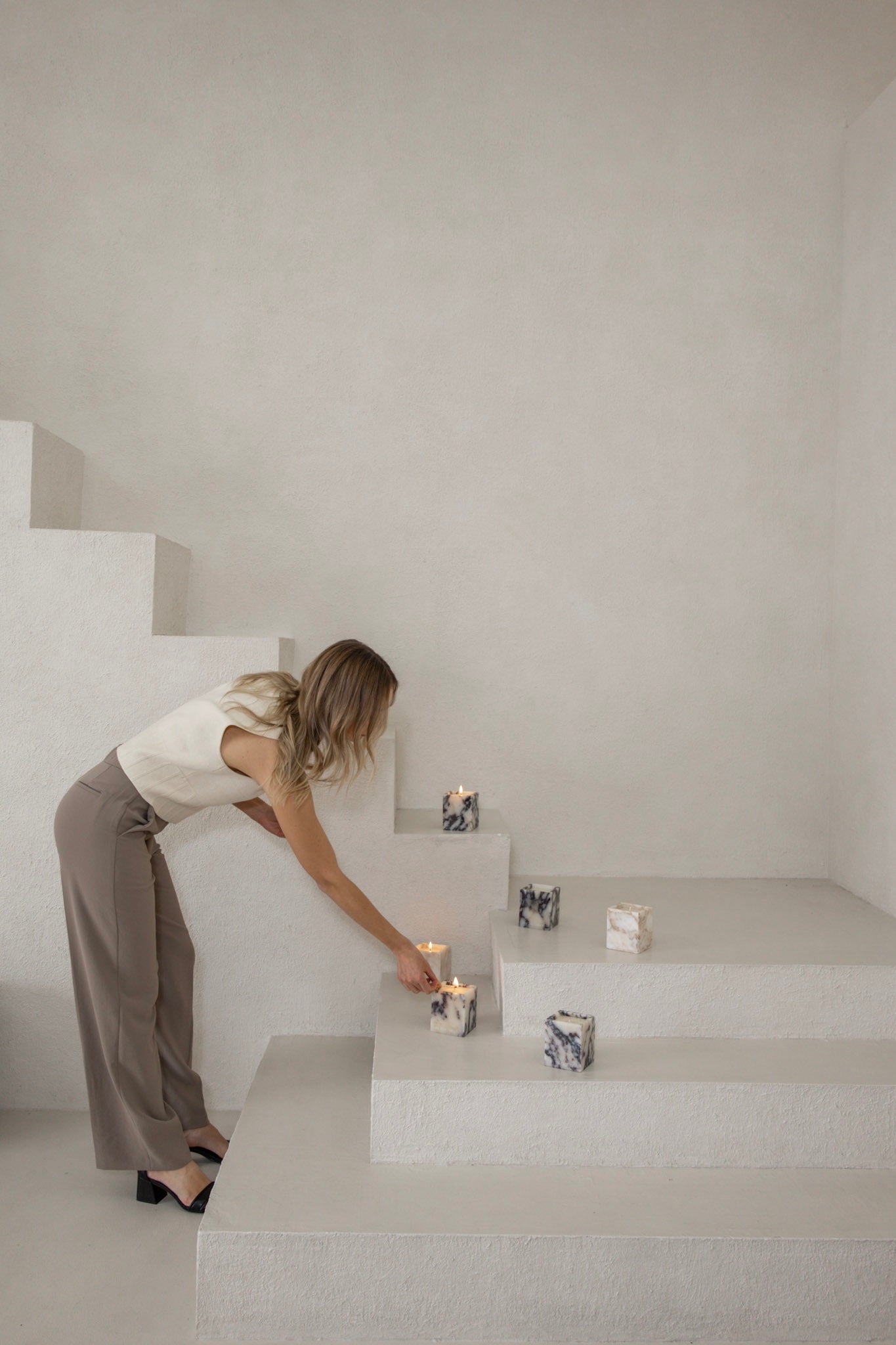 Woman arranging candles on a staircase in a minimalistic setting