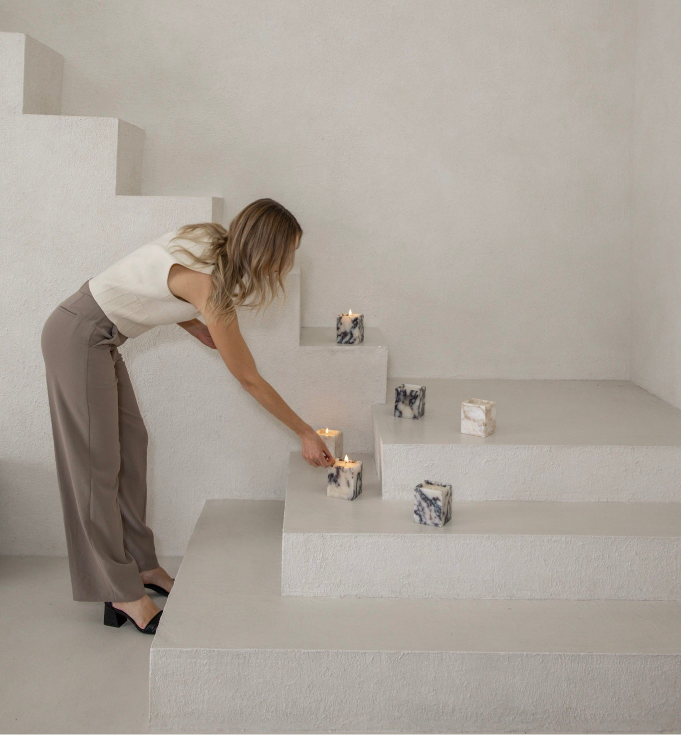 Woman arranging candles on a staircase in a minimalistic setting